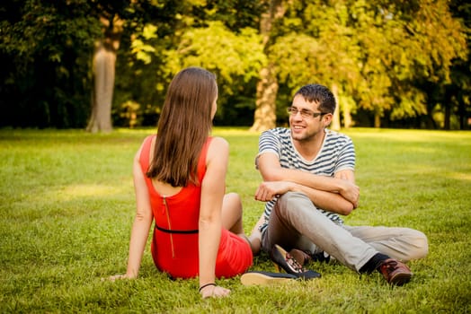 Young smiling couple sitting on grass in park and talking