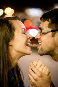 Young couple eating together one piece of chocolate - in street at night