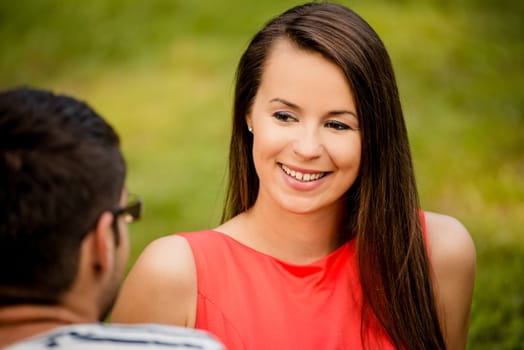 Couple sitting on grass in park and talking - view on woman