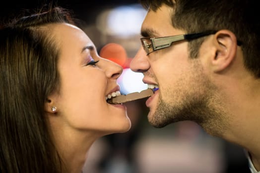 Young couple eating together one piece of chocolate - in street at night