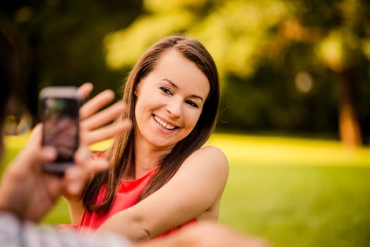Young man taking photo of her girlfriend with mobile phone in nature