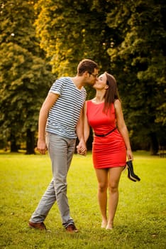 Couple walking and kissing in nature - woman is barefoot holding high heels shoes
