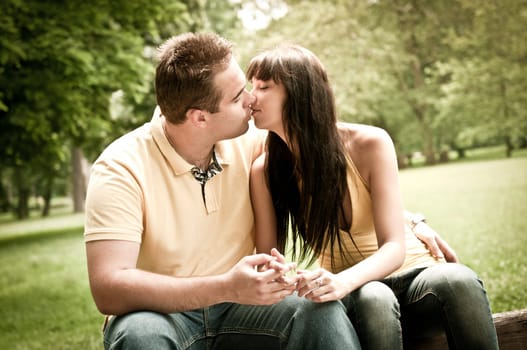 Young couple in love kissing outdoors - sitting on bench