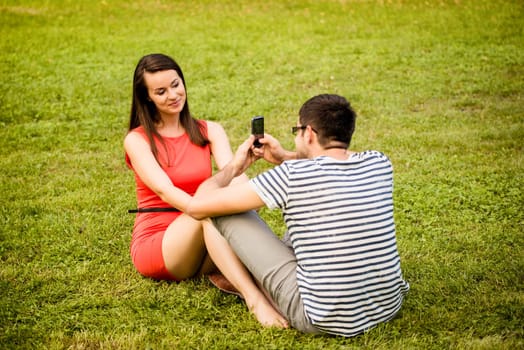 Young man taking photo of her girlfriend with mobile phone in nature