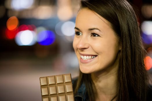 Young woman eating chocolate in street with neon lights at night