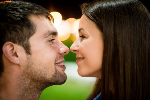 Romantic young couple on date in street at night touching with noses