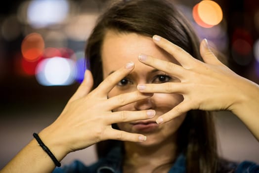 Portrait of young woman outdoor in night street with hands through face