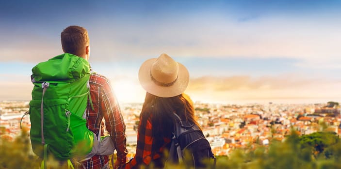 Hikers with backpacks looks on cityscape from top of the mountain. Summer hiking. Hike adventure of young man and woman