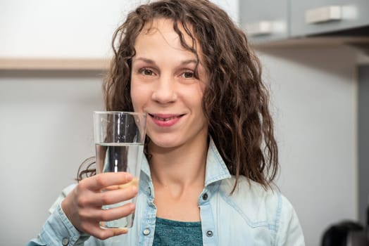 Lifestyle portrait of long haired beautiful girl drinking glass of  water
