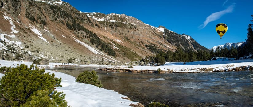 river in the snowy Pyrenees mountains with a yellow hot air balloon