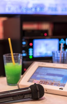 Black microphone in Japanese karaoke club, with remote controller, soda drinks and TV screen for singing music on stage party.