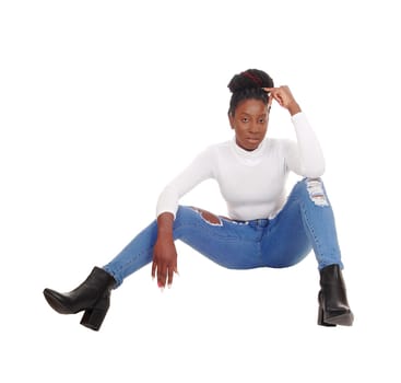 A beautiful tall African American woman sitting in jeans and white top.on the floor in the studio, isolated for white background.