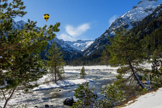river in the snowy Pyrenees mountains with a yellow hot air balloon
