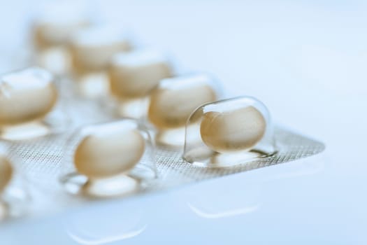 Single sharply illustrated tablets in a foil packaging with other tablets isolated on white background with light bottom mirror