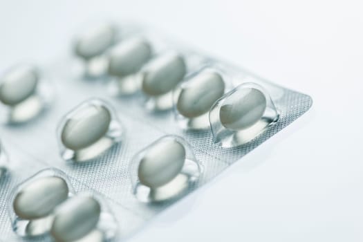 Sliced close-up of a foil packaging with oval tablets on white background with light shadows.