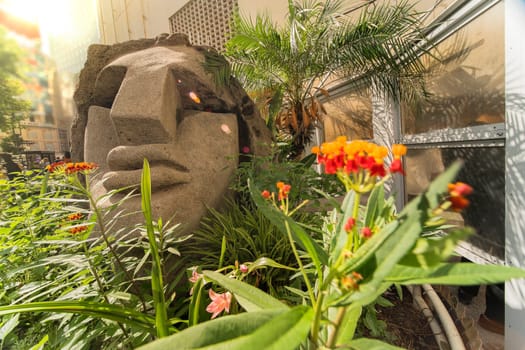 Statue of a Moai head surrounded by tropical flowers at the west exit of Shibuya Station in Tokyo, Japan. This statue was donated in 1980 by the prefecture of Nijima island of Izu archipelago to commemorate the 100 years of the transfer of the island in Tokyo Prefecture.