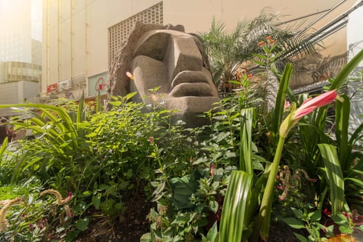 Statue of a Moai head surrounded by tropical flowers at the west exit of Shibuya Station in Tokyo, Japan. This statue was donated in 1980 by the prefecture of Nijima island of Izu archipelago to commemorate the 100 years of the transfer of the island in Tokyo Prefecture.