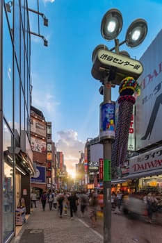 Sunset sky on Shibuya Center Gai Street which literally means Shibuya Central District. The busiest street once intersected with Shibuya Station, it stretches for 350 meters and incorporates the adjacent streets of Bunkamura, Inokashira and Utagawa into its neighborhood. In 2011 the street was renamed Basketball Street in reference to the holy place of Japanese basketball which is the Yoyogi National Gymnasium to which this street leads. The photo is taken in summer at the Tanabata Star Festival where the portal is adorned with paper decorations in the shape of shooting stars for the occasion.