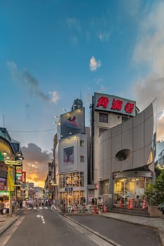 Sunset sky on owl iron mask Shaped of Shibuya Police Station Udagawa Kōban designed by architect Edward Suzuki and opened in April of 1985 in the Inokashira Steet of Shibuya Center Gai which literally means Shibuya Central District. The busiest street once intersected with Shibuya Station, it stretches for 350 meters and incorporates the adjacent streets of Bunkamura, Inokashira and Utagawa into its neighborhood. In 2011 the street was renamed Basketball Street in reference to the holy place of Japanese basketball which is the Yoyogi National Gymnasium to which this street leads. The photo is taken in summer at the Tanabata Star Festival where the portal is adorned with paper decorations in the shape of shooting stars for the occasion.