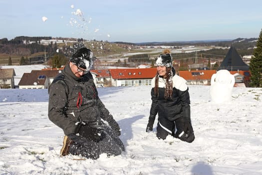 A young couple have a snowball fight in winter. A woman and a man have fun in the snow