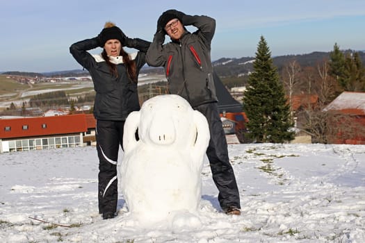 A couple have built a snowman. A woman and a man built an Enton out of snow
