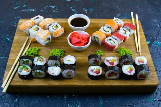 Top view of wooden platter with great set of delicious Nigiri sushi and Tempura rolls with Maki and Uramaki rolls on an orange background. Front views