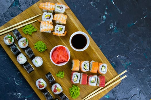 Top view of wooden platter with great set of delicious Nigiri sushi and Tempura rolls with Maki and Uramaki rolls on an orange background. Front views