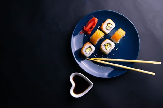 Top view of wooden platter with great set of delicious Nigiri sushi and Tempura rolls with Maki and Uramaki rolls on an orange background. Front views