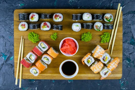 Top view of wooden platter with great set of delicious Nigiri sushi and Tempura rolls with Maki and Uramaki rolls on an orange background. Front views