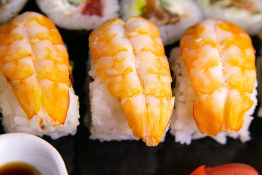 Top view of wooden platter with great set of delicious Nigiri sushi and Tempura rolls with Maki and Uramaki rolls on an orange background. Front views