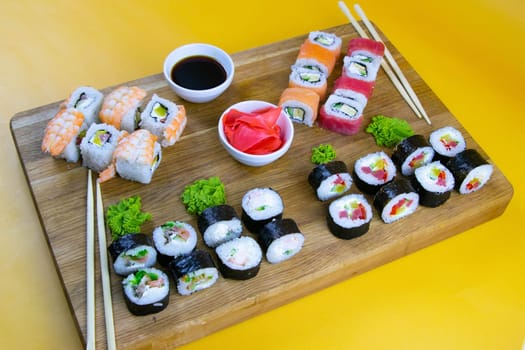 Top view of wooden platter with great set of delicious Nigiri sushi and Tempura rolls with Maki and Uramaki rolls on an orange background. Front views