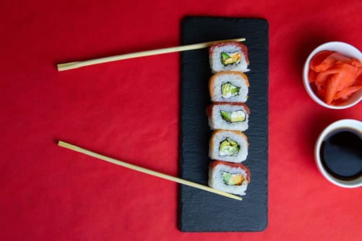 Top view of wooden platter with great set of delicious Nigiri sushi and Tempura rolls with Maki and Uramaki rolls on an rad background. Top views