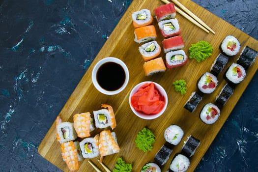 Top view of wooden platter with great set of delicious Nigiri sushi and Tempura rolls with Maki and Uramaki rolls on an orange background. Front views