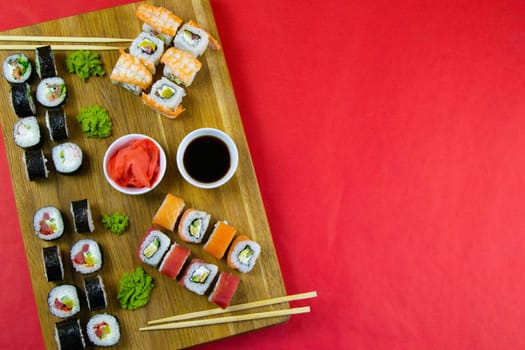 Top view of wooden platter with great set of delicious Nigiri sushi and Tempura rolls with Maki and Uramaki rolls on an orange background. Front views
