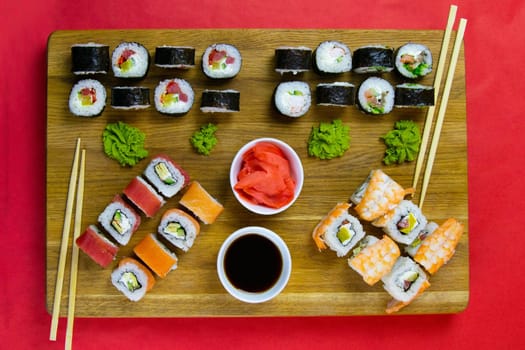 Top view of wooden platter with great set of delicious Nigiri sushi and Tempura rolls with Maki and Uramaki rolls on an rad background. Top views