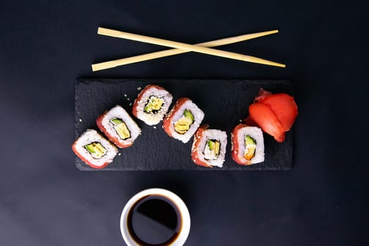 Sticks to reach for the roll, roll in the piece of packaging, next to the role of pickled ginger, everything stands on a red background. Top views