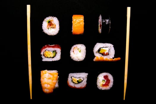 A set of rolls of different kinds with sushi sticks isolated on a black background. Top views