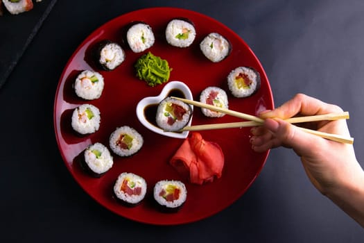 Sticks to reach for the roll, roll in the piece of packaging, next to the role of pickled ginger, everything stands on a red background. Top views