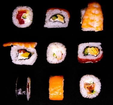 A set of rolls of different kinds with sushi sticks isolated on a black background. Top views