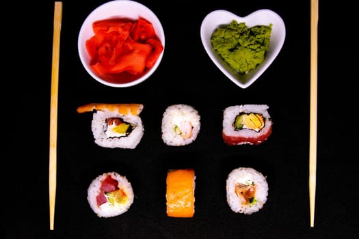 A set of rolls of different kinds with sushi sticks isolated on a black background. Top views