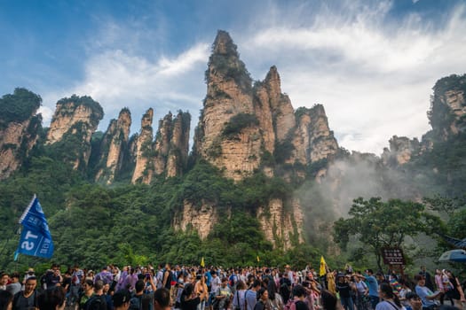 Zhangjiajie, China - August 2019 : Massive tourist crowds on the square at the bottom of Bailong Elevator lift with the Soldiers Gathering peaks behind, Avatar mountains nature park
