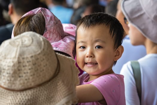 Zhangjiajie, China - August 2019 :  Little chinese girl held by her mother standing in a queue at the Wullingyuan entrance to the Zhangjiajie national park, Hunan Province