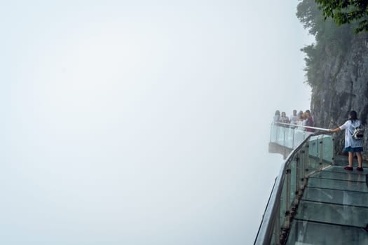 Zhangjiajie, China -  August 2019 : Tourists walking on a narrow glass pathway in Tianmenshan nature park