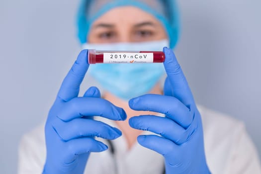 Nurse holding test tube with Positive Coronavirus test blood sample. Virus test and research concept. Focus is on blood test tube.