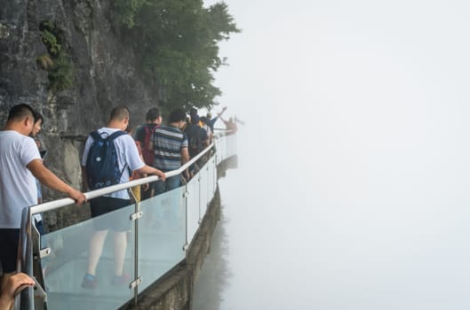 Zhangjiajie, China -  August 2019 : Tourists walking on a narrow glass pathway in Tianmenshan nature park