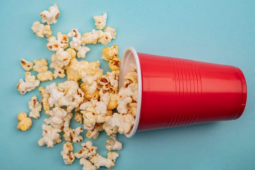 Crunchy Popcorn in plastic cup on bright blue background