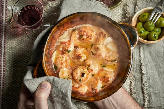 Chef serving a dish of scampi in savory sauce with fresh herbs and spices in an overhead view of his hands over a rustic table