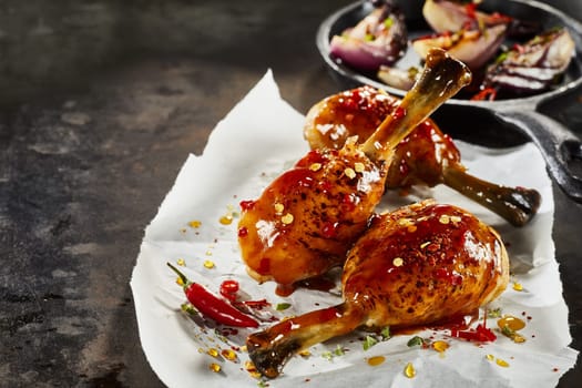 Grilled spicy chicken drumsticks with chilli sauce, fresh herbs and spice seasoning on crumpled white paper suitable for menu advertising