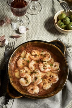 Hot spicy Spanish Gambas piri-piri or scampi peri peri served on a rustic table in a pan with glass of red wine in a top down view