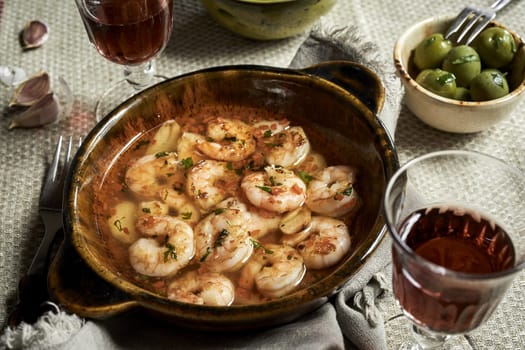 Traditional Andalusian scampi with garlic or Gambas al ajillo served with a glass of red wine and olives viewed high angle close up